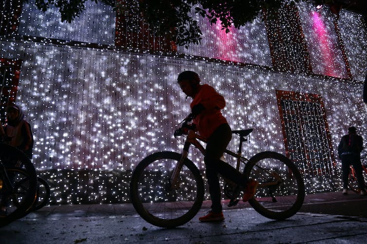 Person rides bike in front of hanging lights.