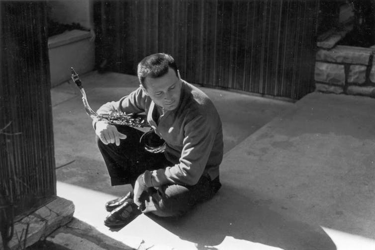 Man seated, looking away from the camera, cradling a saxophone.