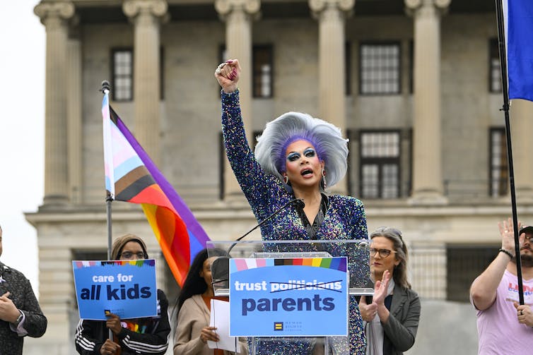 A person with fist raised, speaking in public outside a columned building.