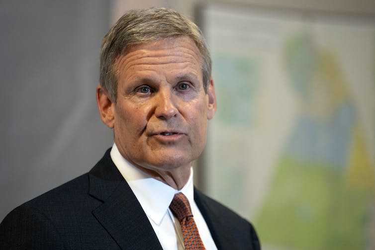 A gray-haired man in a dark blazer, white shirt and red tie.