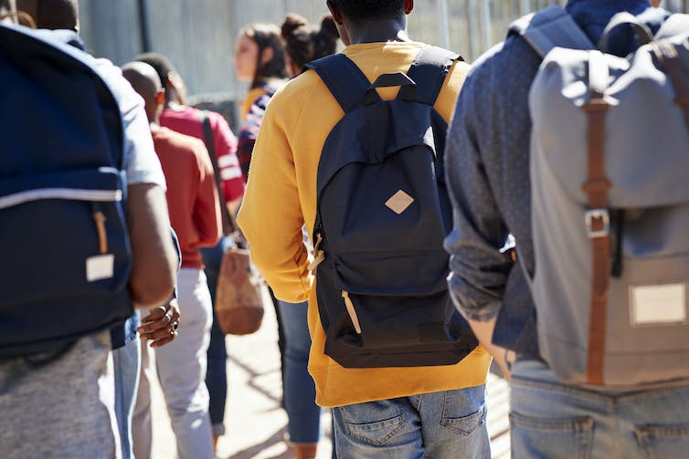 Several college students shown from behind carrying backpacks.