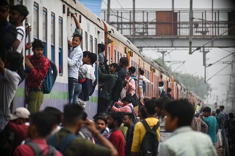 People are seen on a platform and hanging out of doorways on a train car.