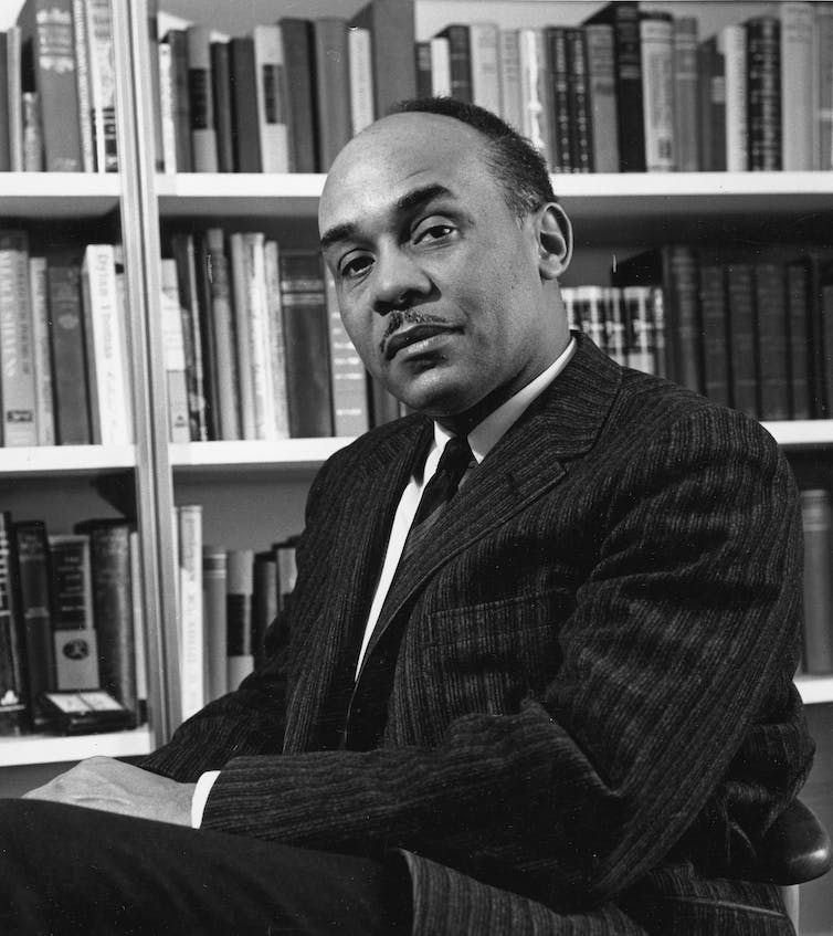 A black-and-white portrait of a man in front of a shelve of books.