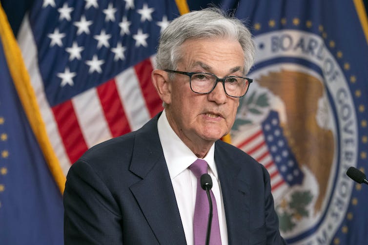 A man stands before a podium in front of U.S. and fed flags at a press conference