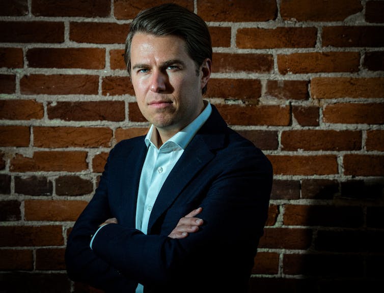 Man in suit jacket poses with folded arms.