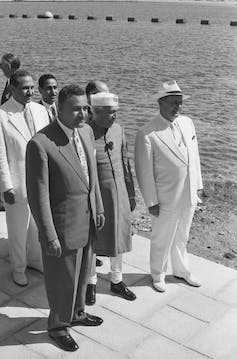 Men in suits stand by the coast.