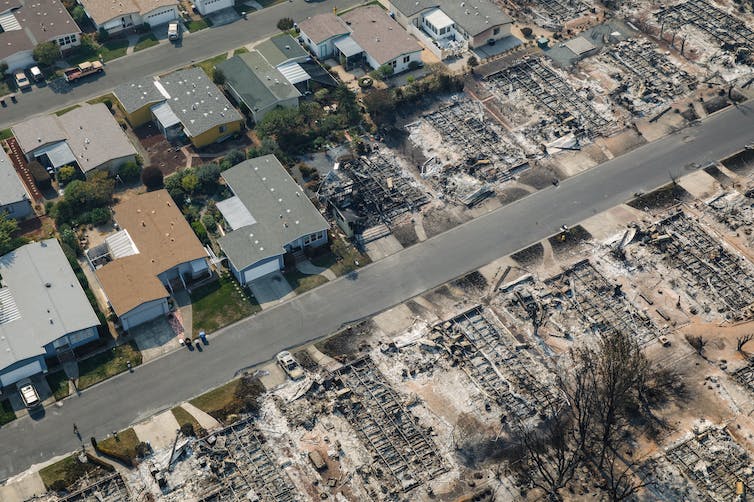 An aerial view of a community of small, closely built houses, with half the homes in the photo burned.