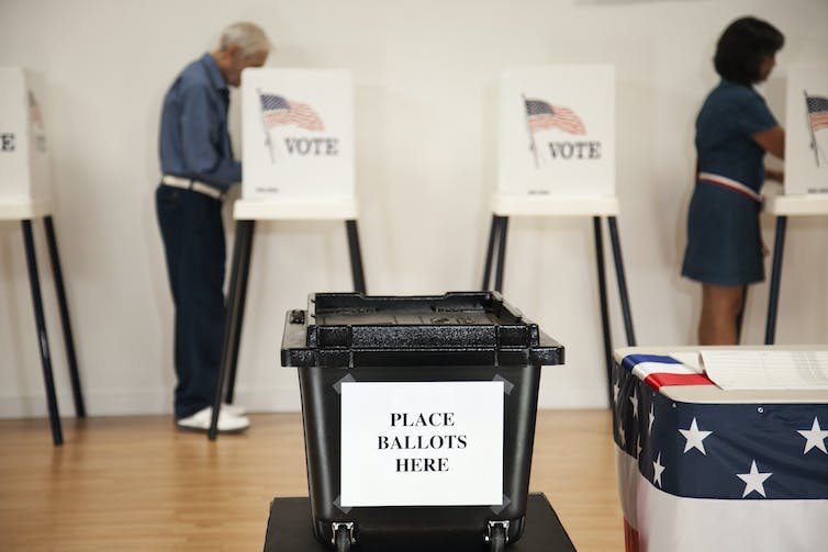 Voters cast their ballots at separate cubicles behind a box labeled Place Ballots Here.