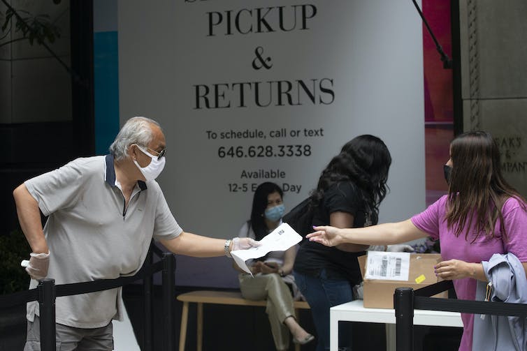 A man hands a slip of paper to a woman a returns desk at Saks Fifth Avenue.