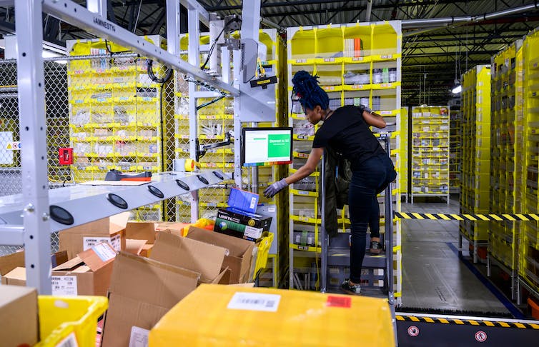 A woman standing a computer terminal checks boxes on an assembly line.