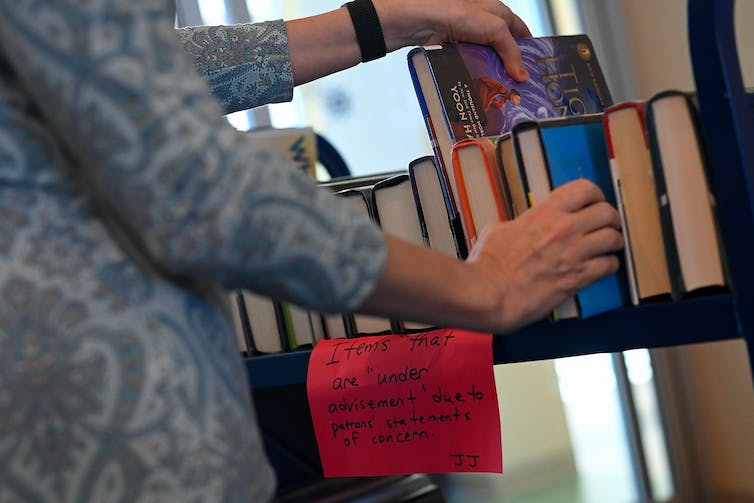 A woman stands next to a book car and touches some of the books.