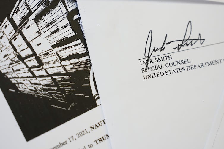 A photo illustration shows a black and white photo of office boxes, next to a paper that has the signature and name of Jack Smith, special counsel of the U.S. Department of Justice.