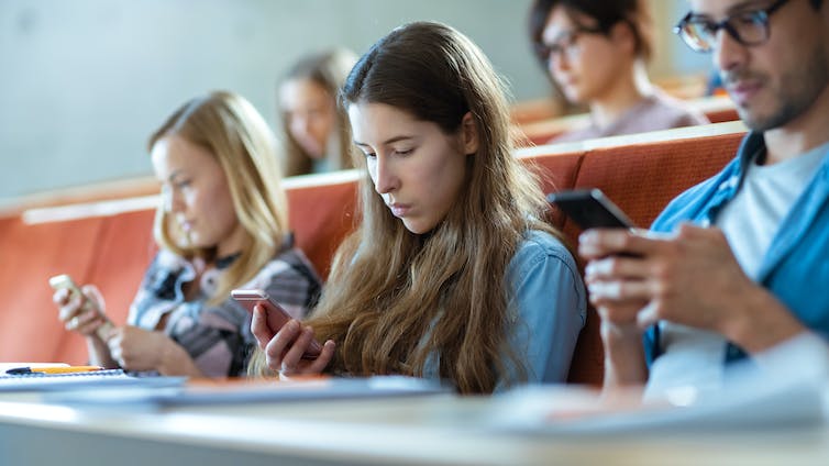 A group of kids in a classroom look at their phone.