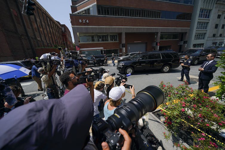 A group of people with cameras in a parking lot near a number of office buildings.