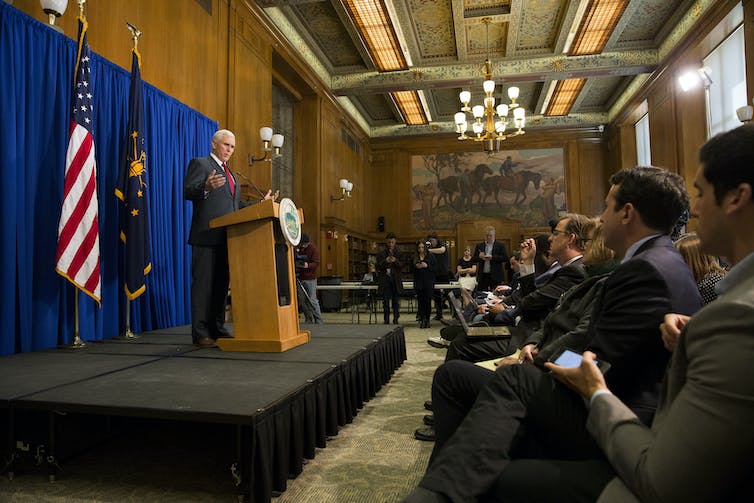 A man in a suit stands at a lectern in front of a group of people.