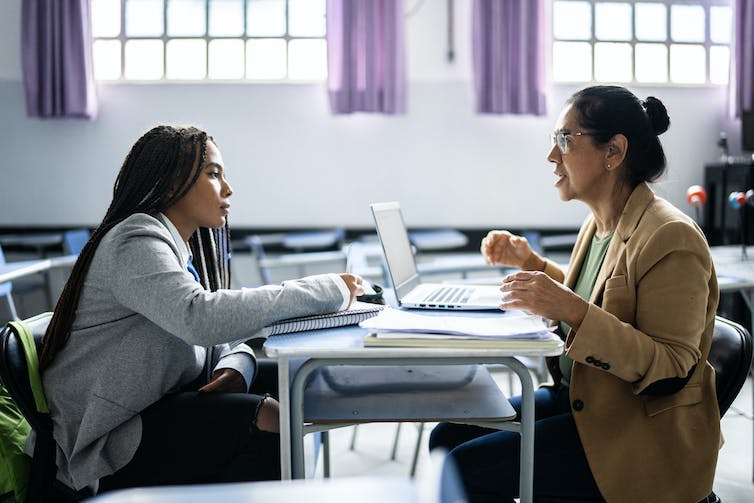 A student meets with their professor in a classroom.