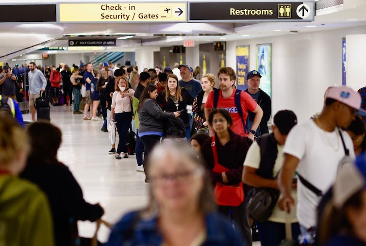 Glum-looking people in an airport terminal stand in a line that snakes out of the frame.