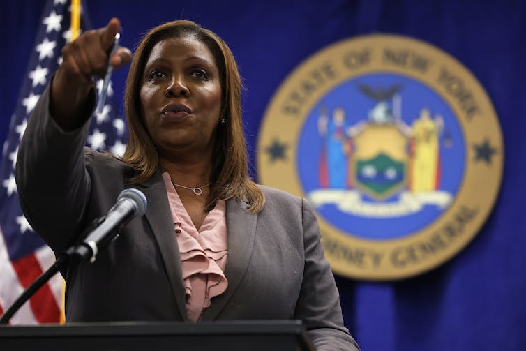 A Black woman stands in front of the American flag and the state of New York's emblem.