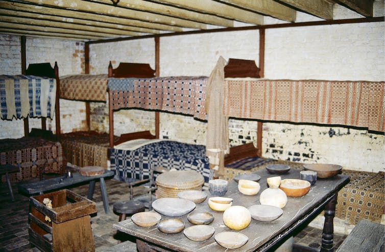 A row of beds lines a wall in a room that has a table covered with different shaped bowls.