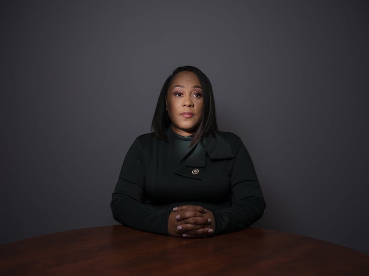 Fanni Willis looks straight ahead at the camera and sits at a wooden table.