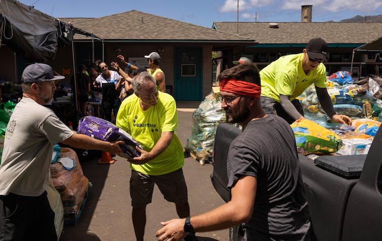 A man hands a big bag of pet food to someone wearing a 'volunteer' t-shirt.