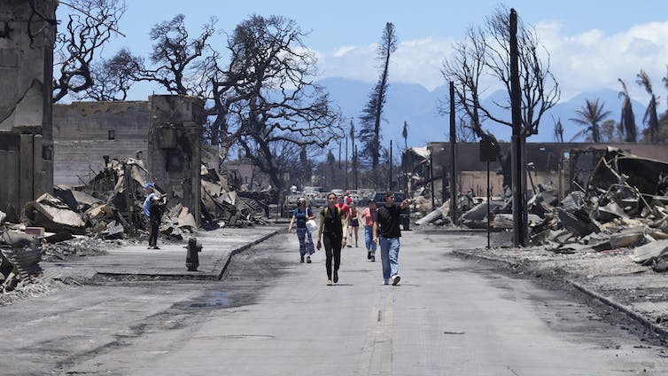 People walking down street past the rubble of wildfire damage in Lahaina