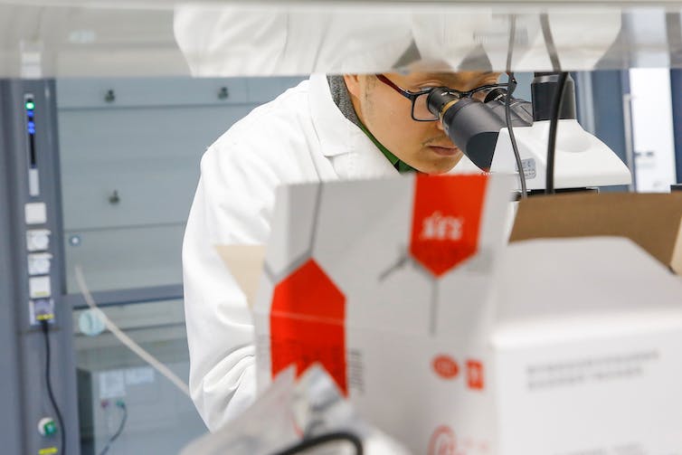 A man with glasses and a lab coat looks into a microscope.