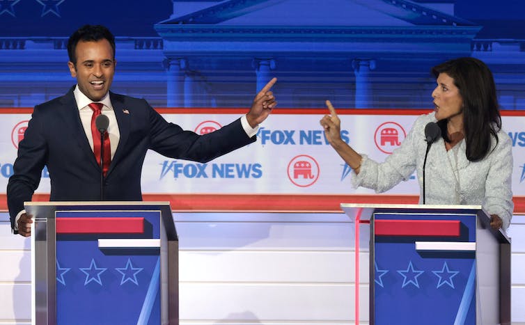 Two people arguing at podiums and pointing at each other.