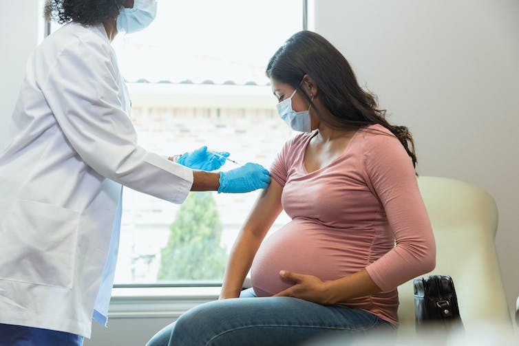 A pregnant mother gazes down at her arm as she receives a shot from a medical provider.