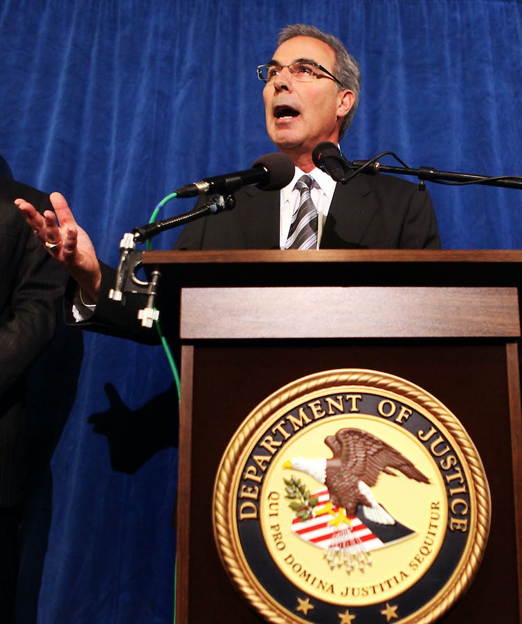 A man stands at a lectern and gestures with one hand.