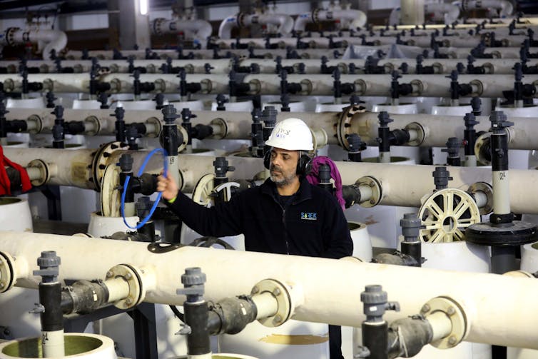 A worker in a hard hat surrounded by valves, adjusting one.