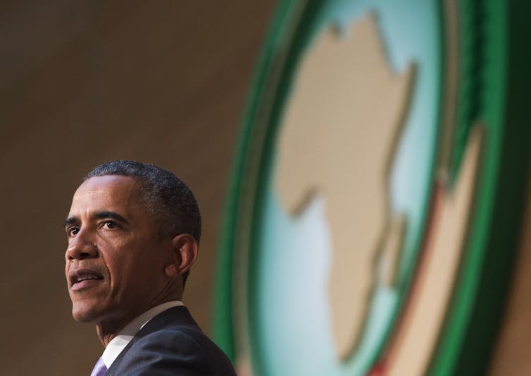 A man in a suit stands in front of a map of Africa.