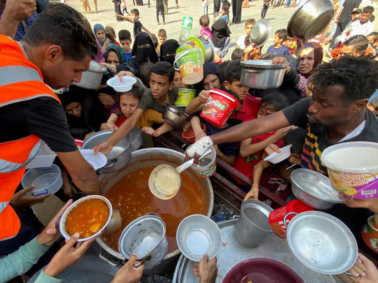 Palestinians, who fled their houses due to Israeli strikes, gather to get their share of charity food, in Rafah