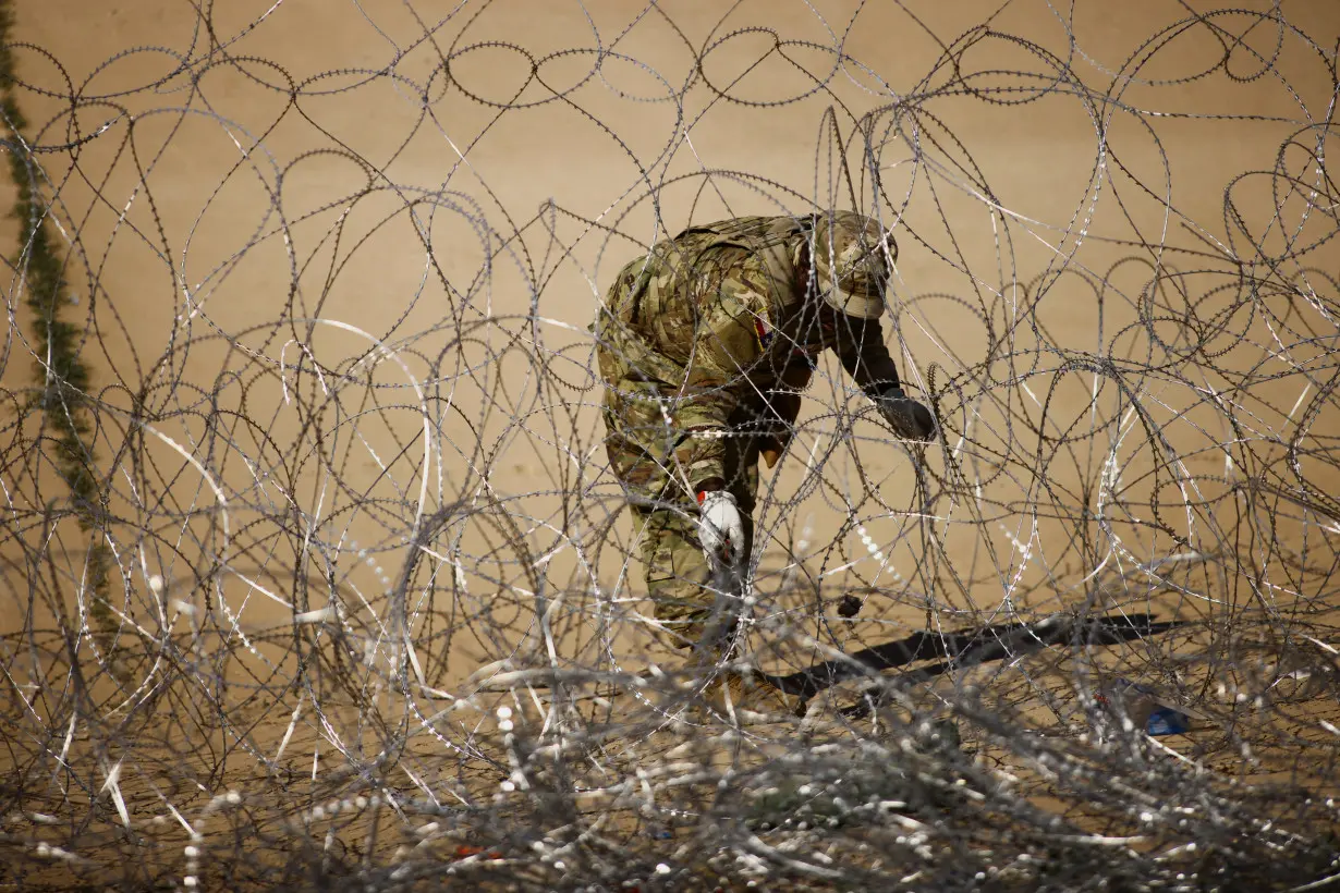 A member of the Texas National Guard works on a razor wire fence near a border wall on the banks of the Rio Bravo River, as seen from Ciudad Juarez