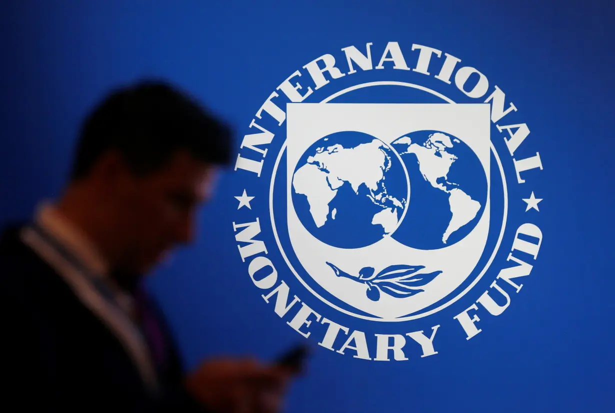 A participant stands near a logo of IMF at the International Monetary Fund - World Bank Annual Meeting 2018 in Nusa Dua