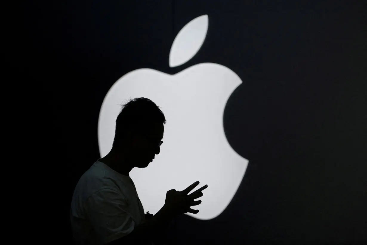 FILE PHOTO: A man check his phone near an Apple logo outside its store in Shanghai