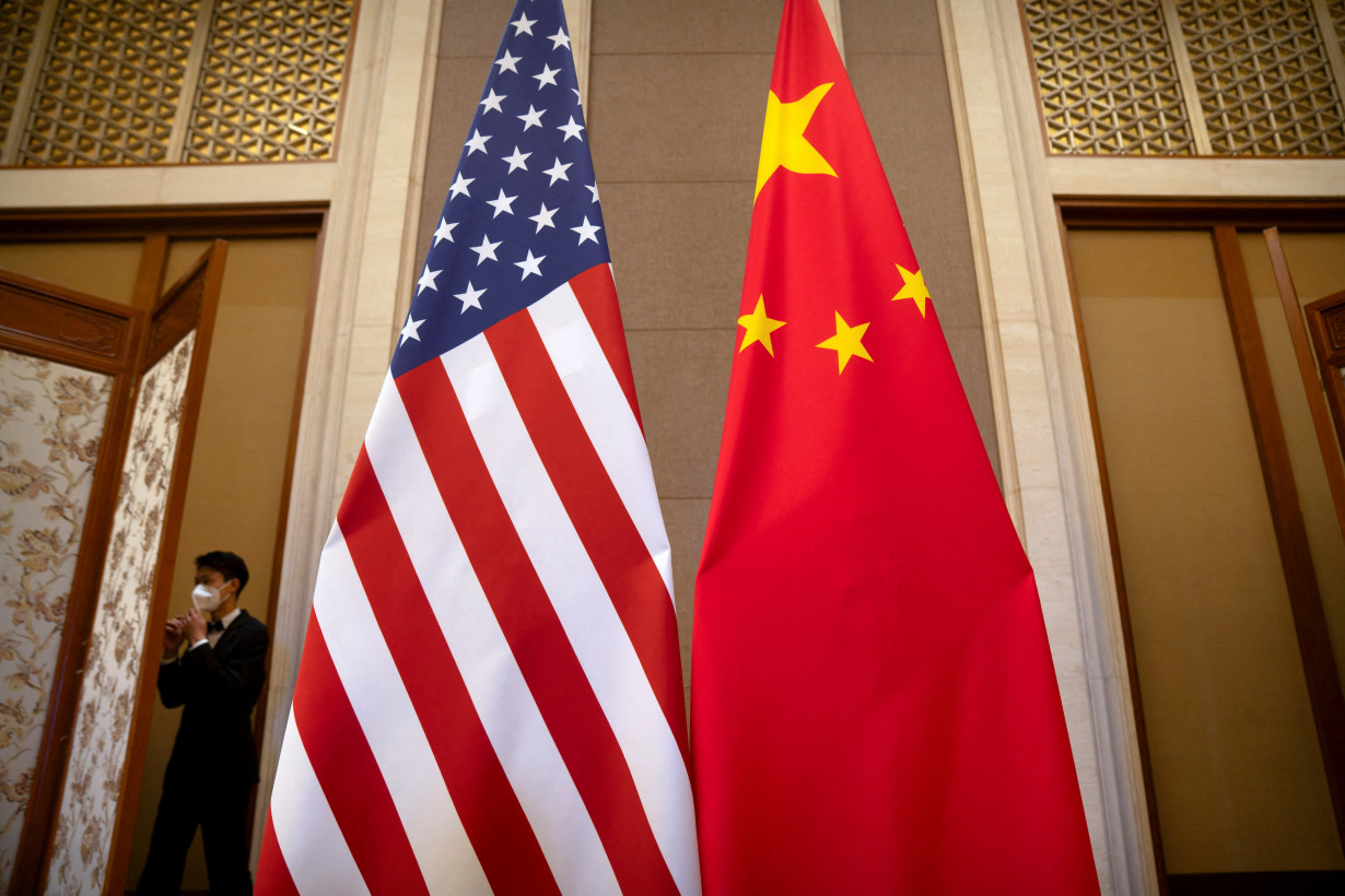 FILE PHOTO: A staff member wearing a face mask walks past United States and Chinese flags