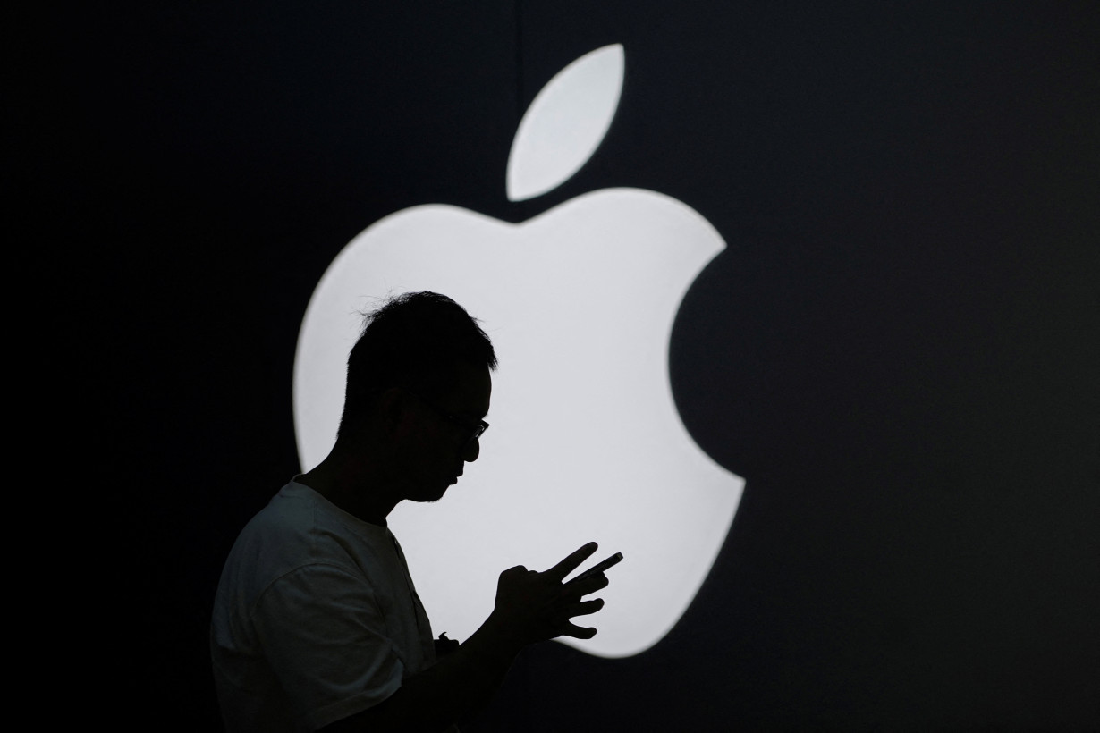 A man check his phone near an Apple logo outside its store in Shanghai