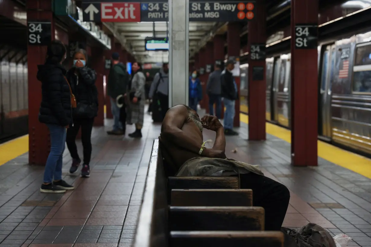 A man sleeps on chairs, in between subway platforms, at the 34th street and Broadway station in New York Cit