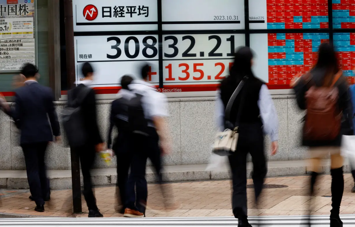 FILE PHOTO: Pedestrians walk past an electronic board displaying Nikkei share average, outside a brokerage in Tokyo