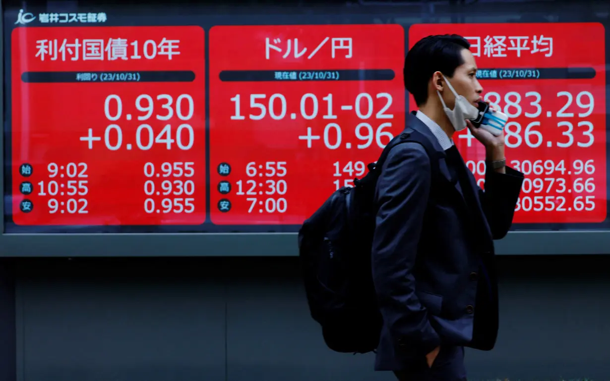 A man walks past an electronic board displaying Japan's 10-year government bonds level, the current Japanese Yen exchange rate against the U.S. dollar and Nikkei share average, in Tokyo