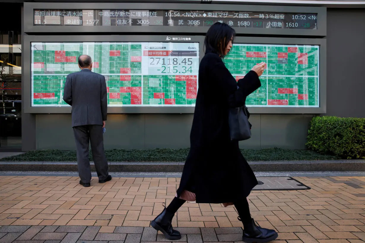 FILE PHOTO: A woman walks past a man examining an electronic board showing Japan's Nikkei average and stock quotations in Tokyo