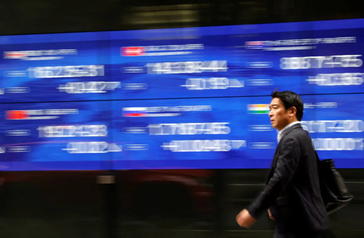 A passerby walks past an electric monitor displaying various countries' stock price index outside a bank in Tokyo