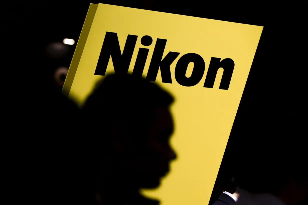 People are silhouetted against a display of the Nikon brand logo at the CP camera and photo trade fair in Yokohama