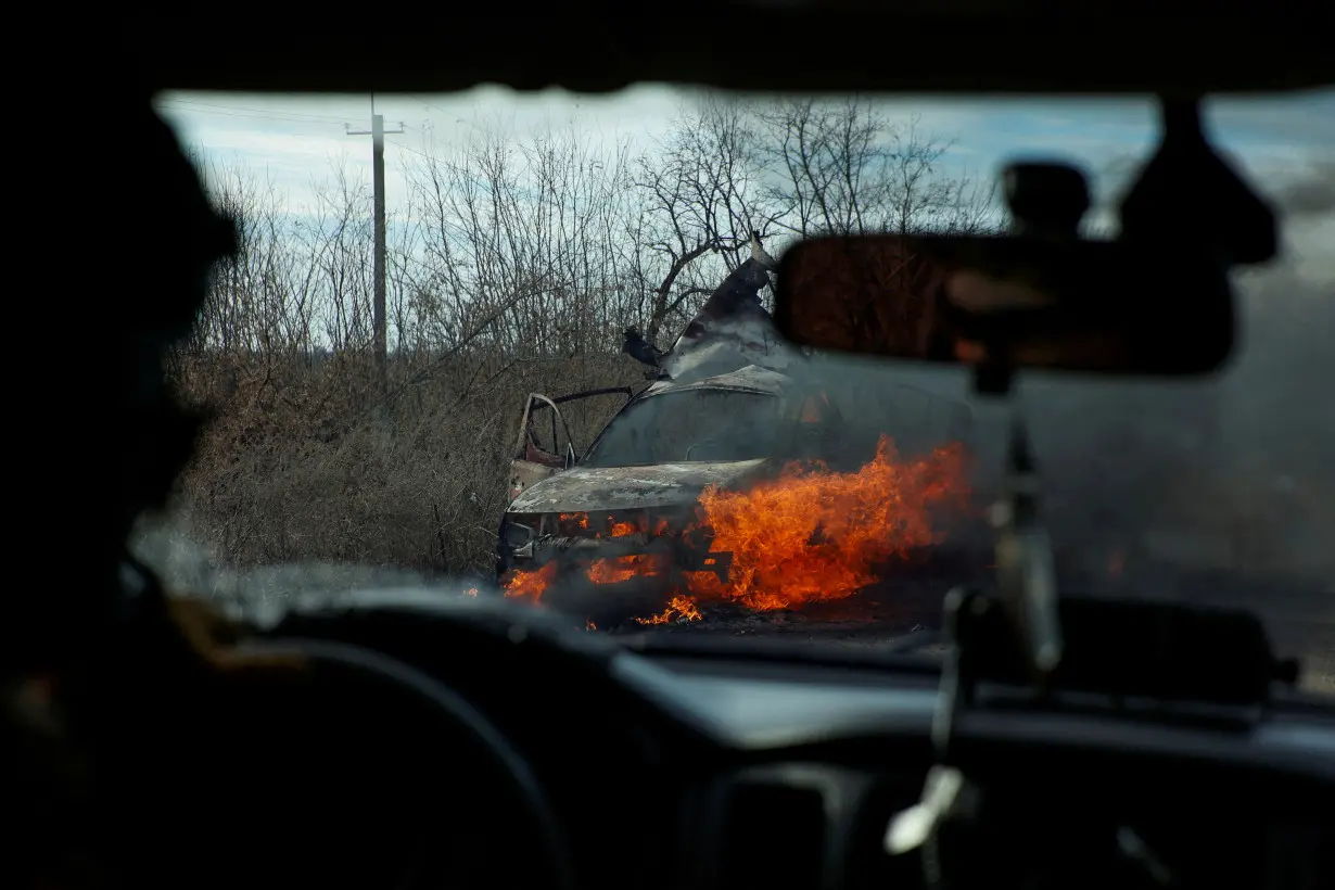 FILE PHOTO: Ukrainian servicemen move past a burning car hit by a kamikaze drone outside the front line town of Avdiivka