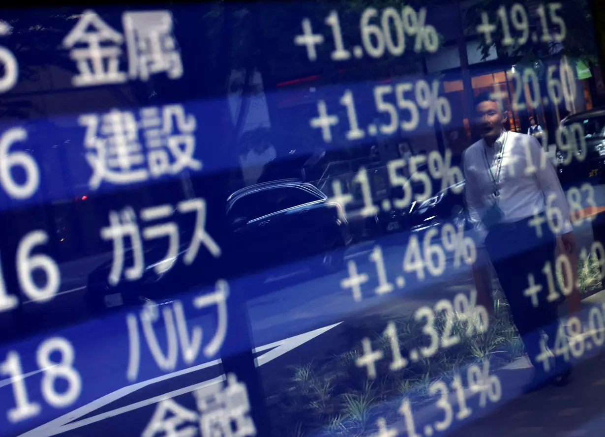 A man is reflected on an electric monitor displaying a stock quotation board outside a bank in Tokyo