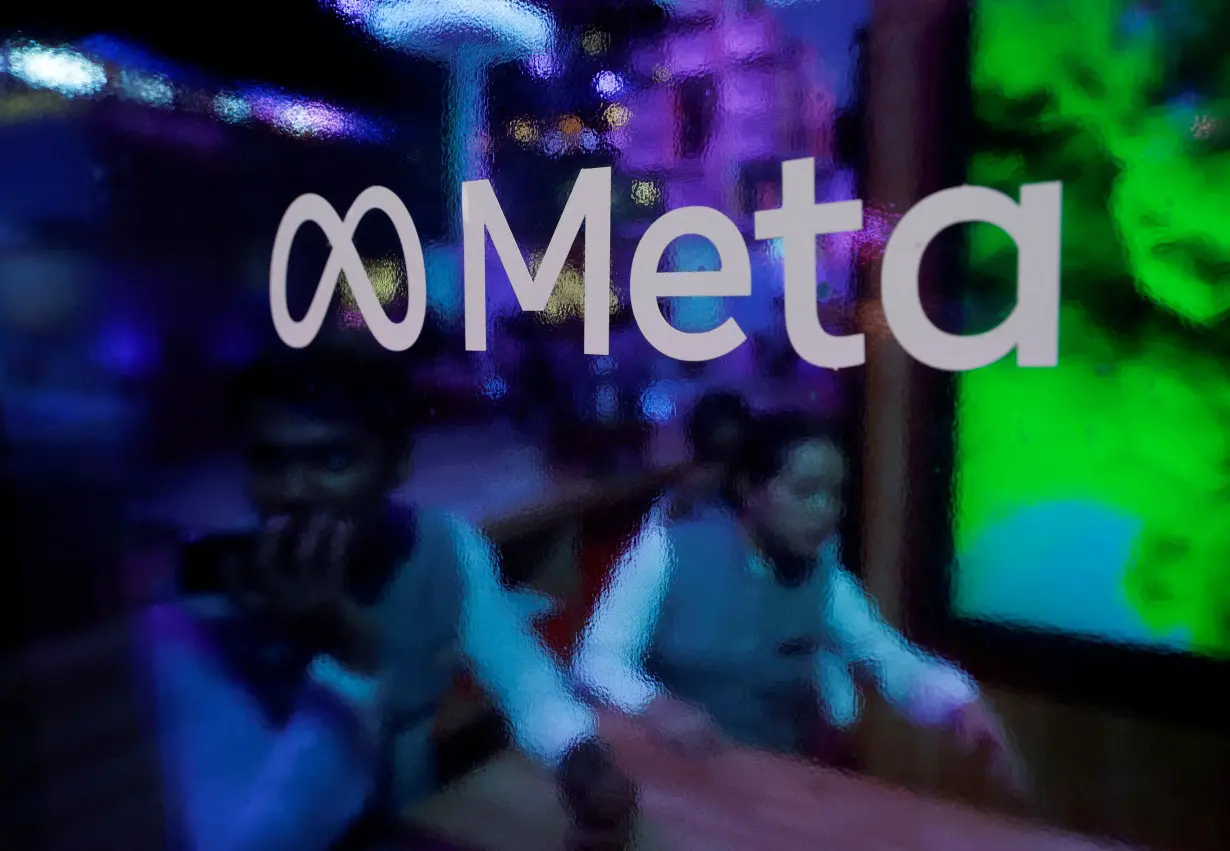 FILE PHOTO: People are seen behind a logo of Meta Platforms, during a conference in Mumbai