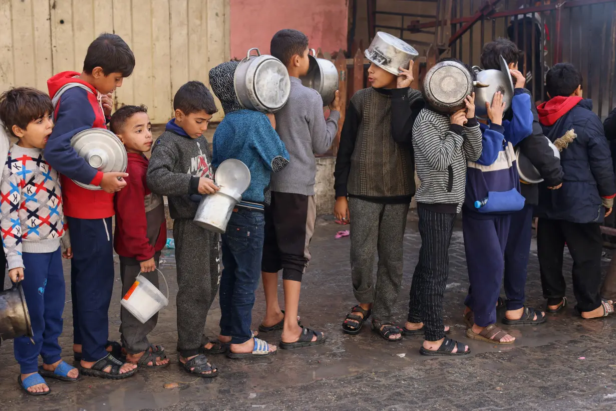 Palestinian children wait to receive food cooked by a charity kitchen, in Rafah