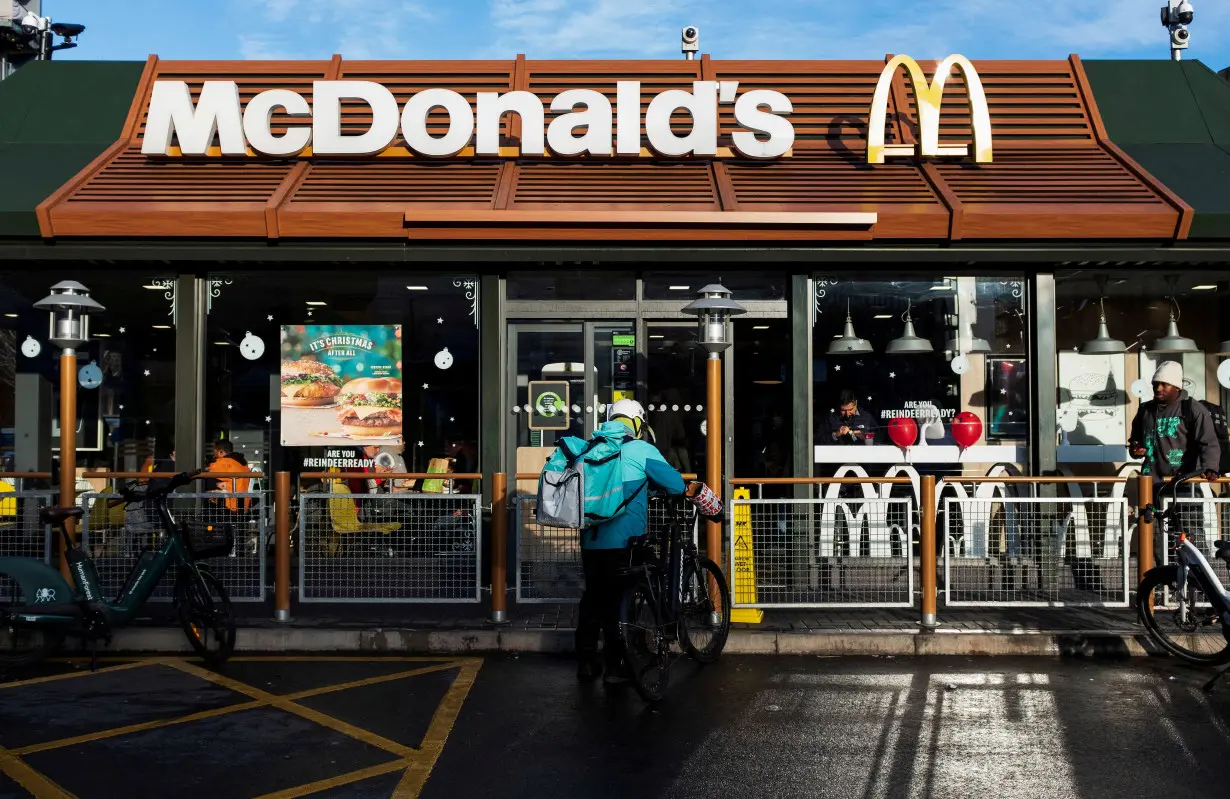 FILE PHOTO: A Deliveroo rider stands beside a bicycle outside a McDonald's restaurant in London