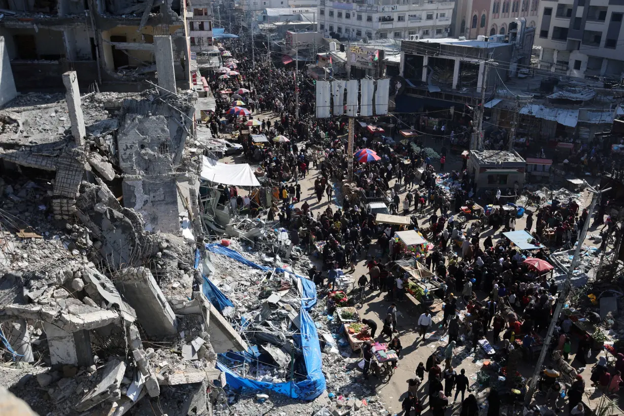 Palestinians shop near the ruins of houses and buildings destroyed in Israeli strikes during the conflict